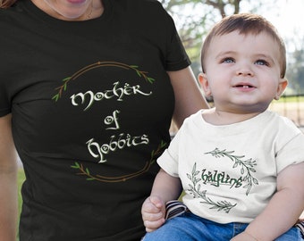 May include: A woman and a child wearing matching black and white shirts with a green leafy design. The woman's shirt says "Mother of Hobbits" and the child's shirt says "Baggins".