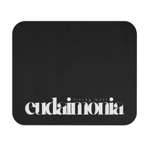 May include: Black rectangular mousepad with rounded corners. The mousepad features the word "eudaimonia" in a stylized white font, with the words "living well" above it.