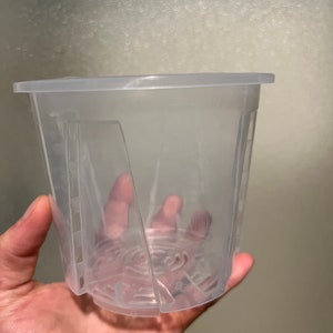 May include: A clear plastic pot with drainage holes. The pot is designed for planting small plants.