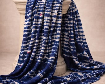 May include: A draped blue and white patterned textile. The fabric is a deep indigo with a white, grid-like pattern. The textile is draped over a white, classical-style pedestal, with the fabric cascading down.