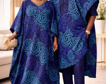 May include: A floor-length blue dress with a V-neckline and a matching blue headwrap, alongside a blue tunic with a buttoned placket, matching trousers, and a small cap. Both garments feature a swirling pattern in shades of navy and cyan.