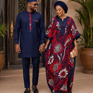 Puede incluir: Una pareja con vestimenta formal. El hombre viste una túnica y pantalón azul marino con detalles rojos y blancos. La mujer lleva un vestido fluido con estampado rojo, blanco y azul marino con un pañuelo a juego. Se toman de la mano.