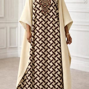 May include: A cream-coloured, long-sleeved dress with a brown geometric pattern. The dress features a V-neck with ornate embroidery and a matching cream-coloured overcoat. The dress is floor-length and has wide sleeves.