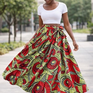 May include: A white crop top paired with a vibrant, flowing skirt. The skirt features a bold pattern of red, yellow, and black swirls and circular designs. The outfit is perfect for a warm day.