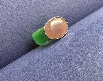 Könnte beinhalten: Ein Ring mit einem hellrosa ovalen Edelstein, der in einer silbernen Fassung sitzt. Der Ring liegt auf einem grünen Untergrund.