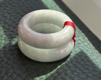 Könnte beinhalten: Zwei Jadeit-Jade-Armbänder, eines auf dem anderen gestapelt, mit einem roten Band um das obere Armband.