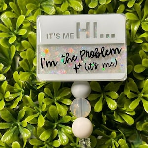 May include: White badge with glitter and the text "It's me Hi... I'm the problem + (it's me)" attached to a white beaded retractable badge reel.