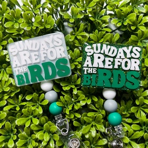 Pu&ograve; includere: Due portabadge con glitter verde e bianco con il testo "Sundays Are For The Birds" su ciascuno. I portabadge hanno perline bianche, grigie e verdi.