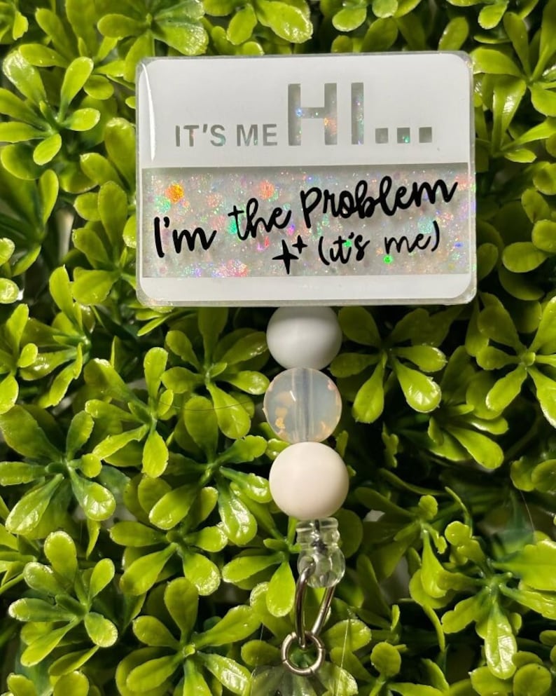 May include: White badge with glitter and the text "It's me Hi... I'm the problem + (it's me)" attached to a white beaded retractable badge reel.