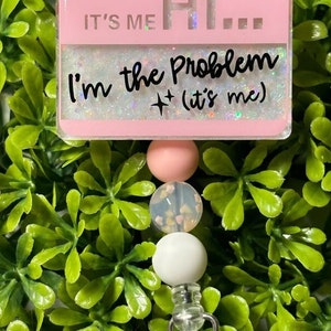 May include: Pink and white beaded retractable badge holder with a pink rectangle charm that says "It's Me Hi... I'm the Problem + (it's me)"