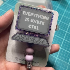 May include: A purple and silver glitter computer-shaped badge holder with the text "EVERYTHING IS UNDER CTRL" on the screen. The badge holder has a purple and silver glitter border and a silver chain with two purple beads.