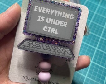 May include: A purple and silver glitter computer-shaped badge holder with the text "EVERYTHING IS UNDER CTRL" on the screen. The badge holder has a purple and silver glitter border and a silver chain with two purple beads.