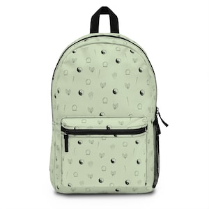 May include: A light green backpack with a black zipper and a black handle. The backpack is covered in a repeating pattern of black yin-yang symbols, leaves, and acupuncture needles. A black mesh pocket is on the side.