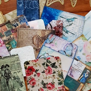 May include: A collection of vintage-style paper ephemera with floral, bird, and geometric patterns. The papers are in various colors, including blue, green, pink, and brown. The papers are arranged in a random pattern on a wooden surface.