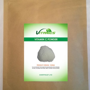 Op de afbeelding: Een bruine papieren zak met een groen en wit etiket. Het etiket leest "VITANICS VITAMIN C POWDER" en bevat een afbeelding van wit poeder. De tekst op het etiket luidt ook "PRODUCT ORIGIN: CHINA".