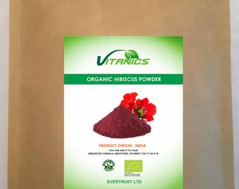 May include: A brown paper pouch featuring a label for Vitanics Organic Hibiscus Powder. The label displays a pile of dark red powder, a red hibiscus flower, the text Product Origin: India, and the company name Evertrust Ltd.