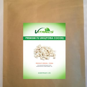 Puede incluir: Una bolsa de papel marrón con una etiqueta verde y blanca. La etiqueta muestra el texto "VITANICS PREMIUM FU LING(PORIA COCOS)" y un montón de piezas blancas y cúbicas. También se ve el texto "PRODUCT ORIGIN: CHINA".