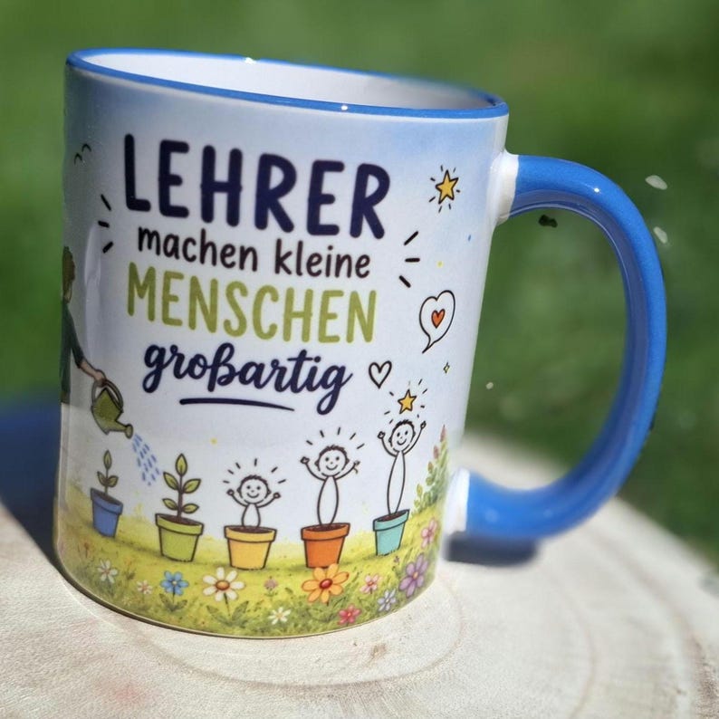 May include: White ceramic mug with a blue handle and rim, featuring the German text "LEHRER machen kleine MENSCHEN gro&szlig;artig" in blue and green. The mug has a design of cartoon plants and people, with a watering can and stars.