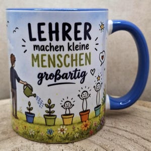 May include: White ceramic mug with a blue handle and rim. The mug features the German text "LEHRER machen kleine MENSCHEN gro&szlig;artig" with illustrations of a person watering plants and children with stars above their heads.