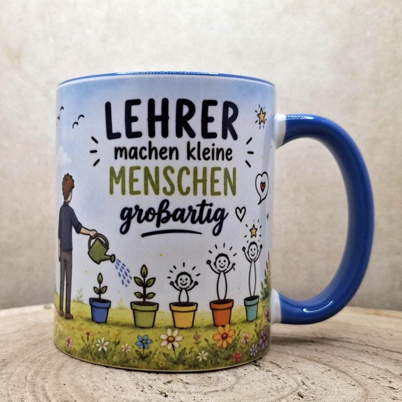 May include: White ceramic mug with a blue handle and rim. The mug features the German text "LEHRER machen kleine MENSCHEN gro&szlig;artig" in black and green, along with illustrations of a person watering plants and happy stick figures.