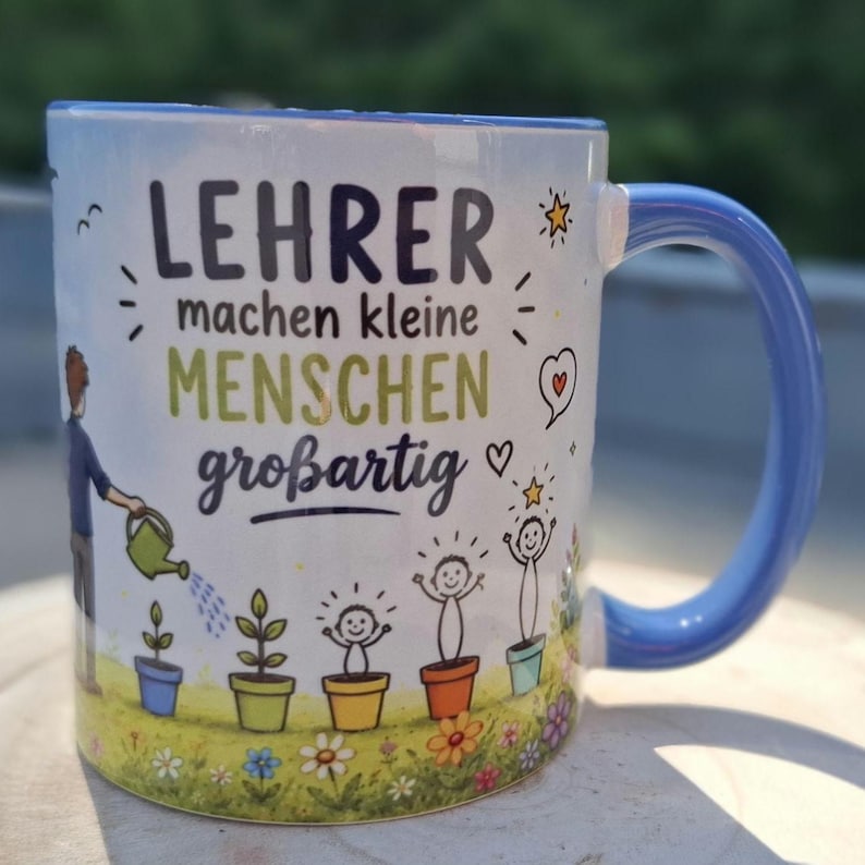 May include: White ceramic mug with a blue handle and rim, featuring the German text "LEHRER machen kleine MENSCHEN gro&szlig;artig" in black and green. The mug has a design of a person watering plants and smiling figures in pots.