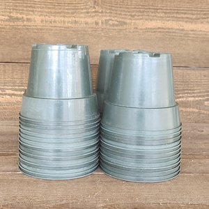 May include: A stack of green plastic plant pots. The pots are cylindrical with a slightly flared top and a series of horizontal ridges around the body. The pots are empty and ready for planting.