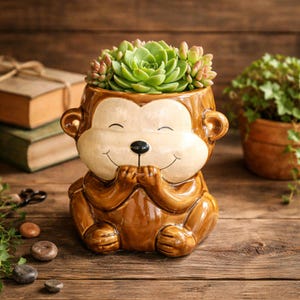 May include: A ceramic monkey-shaped planter with a smiling face, holding its hands together. The planter is filled with a green succulent plant. The monkey planter is brown and cream-colored, with a black nose and small ears. The planter is sitting on a wooden surface.
