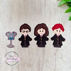 Op de afbeelding: Drie vingerpoppen van vilt van personages uit de Harry Potter-serie. De poppen zijn Harry Potter, Hermelien Griffel en Ron Wemel. De poppen dragen hun Hogwarts-schooluniformen. Er is ook een trofee van vilt met een blauw en zilver ontwerp.
