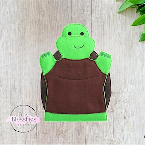 May include: Green felt hand puppet of a turtle with a brown felt shell. The turtle has a smiling face with black eyes and a stitched mouth.