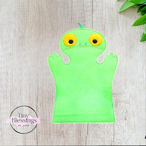 May include: Green felt hand puppet with large yellow eyes and a small green nose. The puppet has two arms and a mouth.
