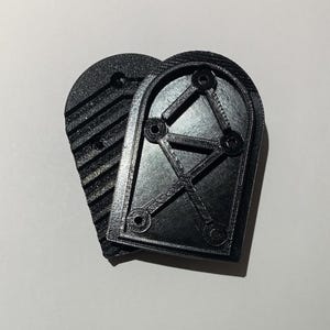 May include: Two black, arched-shaped 3D-printed objects. One has a textured, ridged surface, while the other features an open, geometric design with circular holes. The objects are likely components or parts for a larger item.