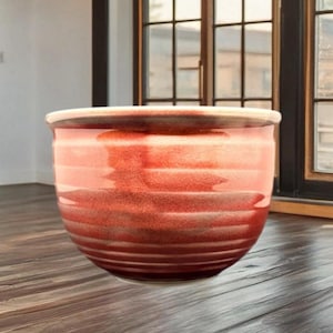 May include: A round, ceramic planter with a reddish-orange glaze. The planter has a wide, open top and a slightly textured surface. The color transitions from light to dark, with horizontal bands. This decorative pot is suitable for indoor or outdoor use.