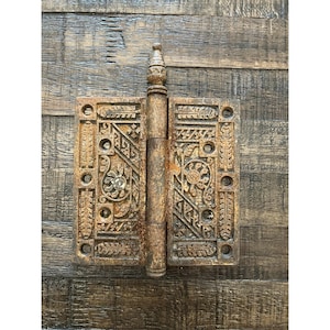 Peut inclure: Charni&egrave;re m&eacute;tallique orn&eacute;e de style antique, avec une finition de couleur rouille vieillie. La charni&egrave;re pr&eacute;sente des motifs floraux et g&eacute;om&eacute;triques d&eacute;taill&eacute;s, un barillet central et un fleuron d&eacute;coratif. Le design sugg&egrave;re une esth&eacute;tique vintage ou rustique.
