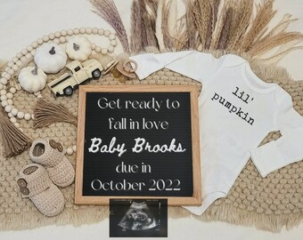May include: A white babygrow with the text "lil' pumpkin" on it, a chalkboard sign that says "Get ready to fall in love Baby Brooks due in October 2022", a small toy truck, white pumpkins, and a pair of crocheted baby booties.