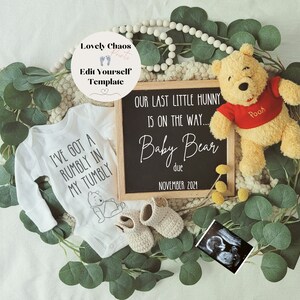 Peut inclure: Un ourson en peluche Winnie l'ourson portant un t-shirt rouge avec le mot "Pooh" dessus. Un panneau d'ardoise indique "Notre dernier petit ch&eacute;ri est en route... B&eacute;b&eacute; ours pr&eacute;vu pour novembre 2021". Une grenouill&egrave;re blanche avec le texte "J'ai un petit creux dans le ventre" et une illustration de Winnie l'ourson sur un fond de feuilles vertes.
