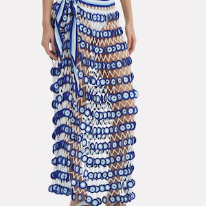 Puede incluir: Falda maxi de crochet blanco con detalles de ojo turco azul y blanco. La falda se ata a la cintura con una cinta a rayas azul y blanca.