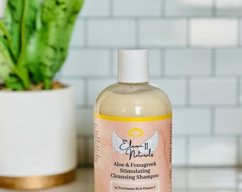 May include: A 12-ounce bottle of Eleven 11 Naturals Aloe & Fenugreek Stimulating Cleansing Shampoo with Provitamin B5 & Vitamin E. The bottle is white with a yellow label featuring a pink angel wing design. The label text reads "Gently removes dirt and build up while nourishing the scalp."
