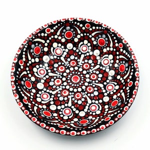 May include: A small black bowl with a red and white mandala design. The bowl is painted with dots and swirls.