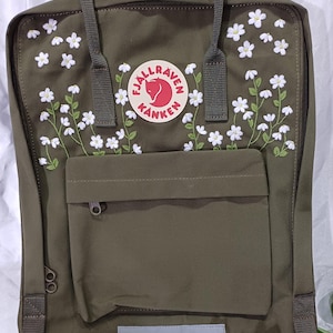 May include: A green Fjällräven Kånken backpack with white embroidered flowers and a red fox logo.