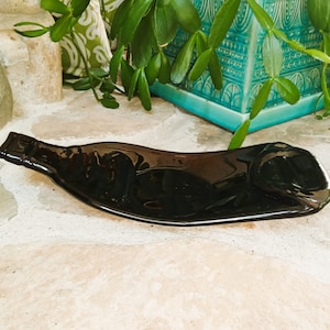 May include: A black glass bottle shaped into a serving dish. The dish is sitting on a light brown surface.