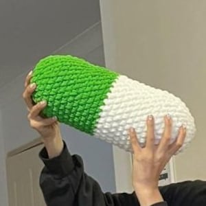 May include: A green and white crocheted pill-shaped pillow. The pillow is about 12 inches long and 6 inches wide.