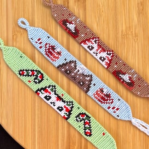 May include: Three friendship bracelets with Christmas-themed designs. The bracelets are made with colourful embroidery floss and feature a snowman, a gingerbread house, and a candy cane.