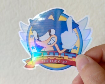 May include: A holographic sticker featuring Sonic the Hedgehog giving the middle finger with the text "SHUT THE FUCK UP" in a red banner.