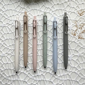 May include: Seven pens with different coloured bodies and silver accents. The pens are arranged in a row on a white surface with a white crocheted background.