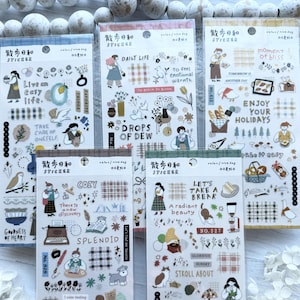 May include: A collection of decorative sticker sheets with various illustrations and text. The stickers feature images of people, animals, and objects, with phrases like "Live an easy life" and "Enjoy your holidays". The color palette includes blues, greens, and browns.