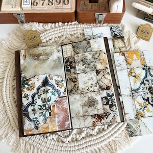 May include: Open journal with a brown leather cover and pages featuring a vintage tile design. The journal is open on a white surface with other stationery items, including stamps, scissors, and a small polar bear figurine.
