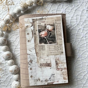 May include: A light brown leather planner with a distressed paper cover featuring a vintage photograph of a rose. The cover has a textured crocodile pattern and is decorated with a collage of old newspaper clippings and ephemera.