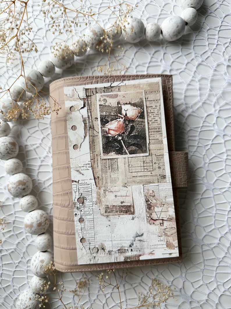 May include: A light brown leather planner with a distressed paper cover featuring a vintage photograph of a rose. The cover has a textured crocodile pattern and is decorated with a collage of old newspaper clippings and ephemera.