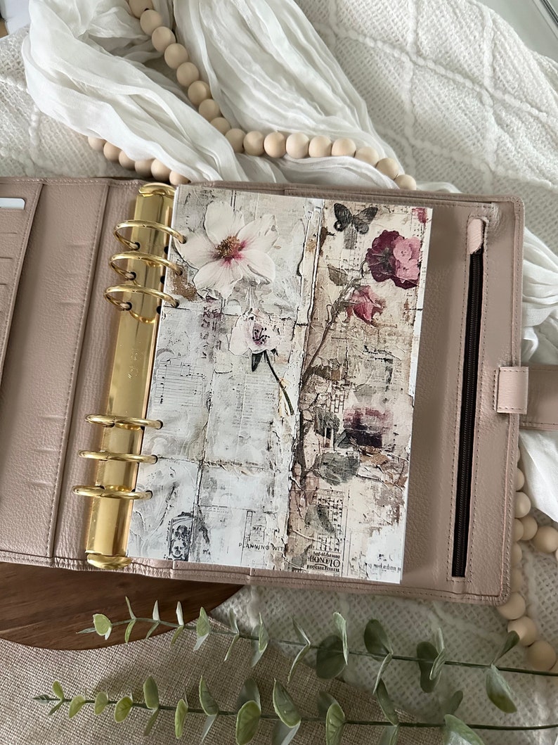 May include: A blush pink leather planner with gold rings and a floral patterned insert. The insert features a white flower, a butterfly, and a pink flower with green leaves.