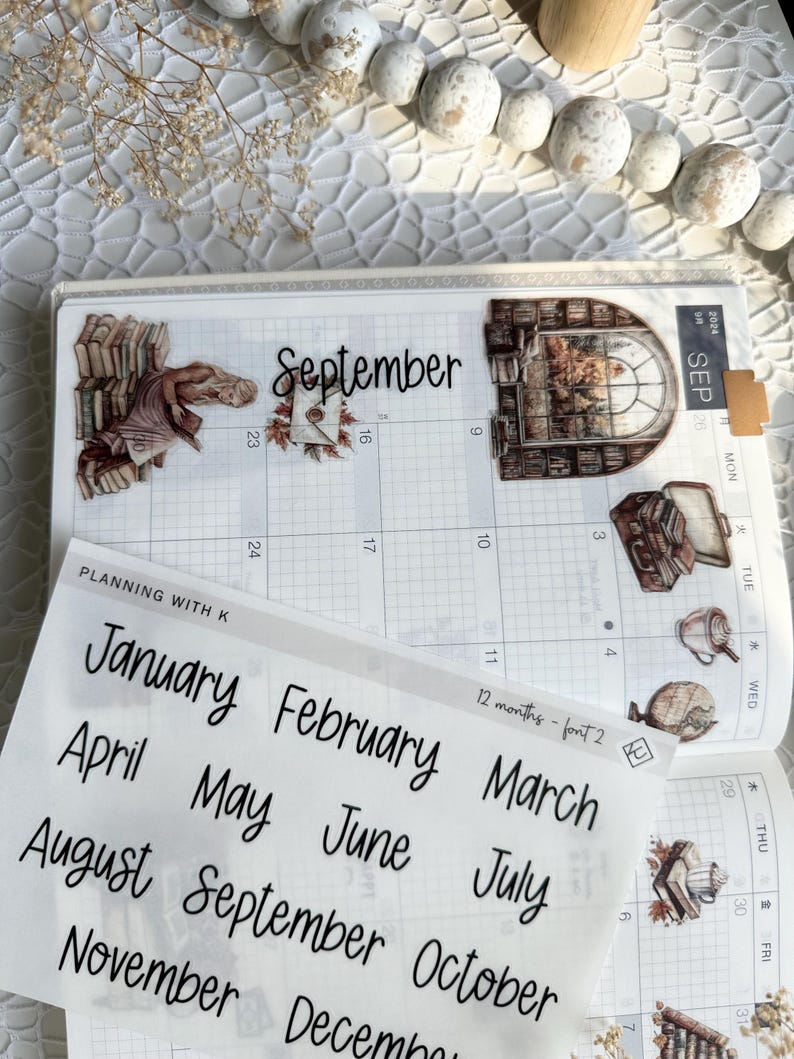 May include: A sheet of clear stickers with handwritten month names in black ink. The stickers are for use in a planner or journal. The month names are January, February, March, April, May, June, July, August, September, October, November, and December.
